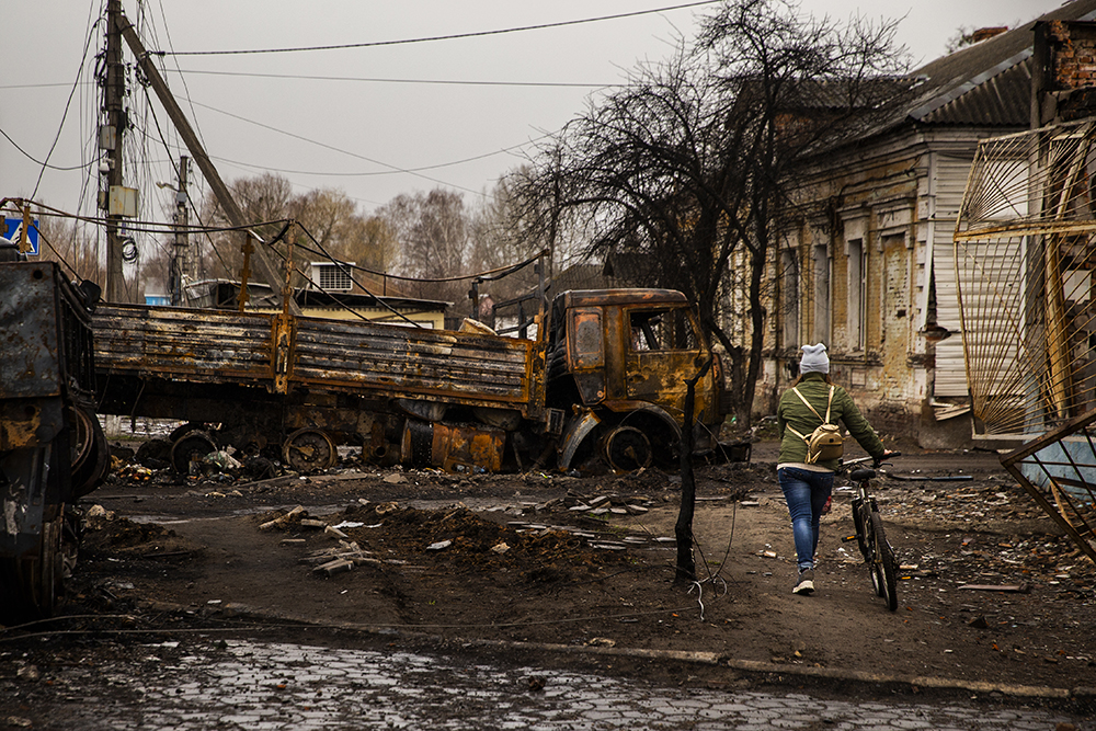 Woman walks bike amid destroyed Russian vehicles at Trostyanets