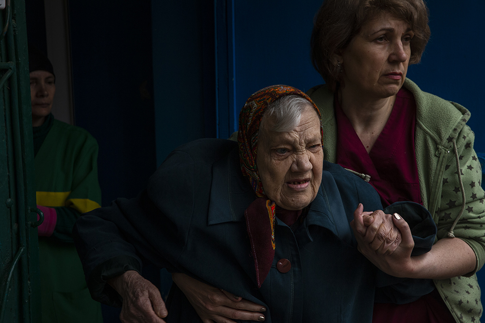 Elderly woman being assisted to a vehicle to evacuate from a care center in Toretsk