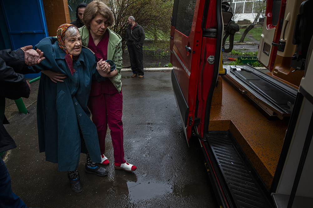 Elderly woman assisted to an evacuation  vehicle at a care  center inToretsk