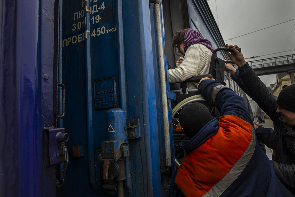 Elderly woman in wheelchair is lifted onto a train to evacuate from Pokrovsk