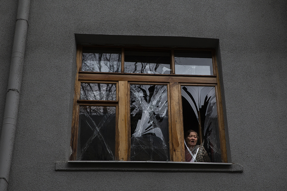 Woman viewing out window broken by Russian shelling in Kharkiv on Easter Sunday